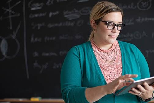 Lehrerin mit iPad vor einer schwarzen Tafel