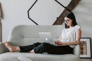 Eine junge Frau sitzt mit ihrem über MDM verwalteten Mac auf dem Sofa und arbeitet im Homeoffice 